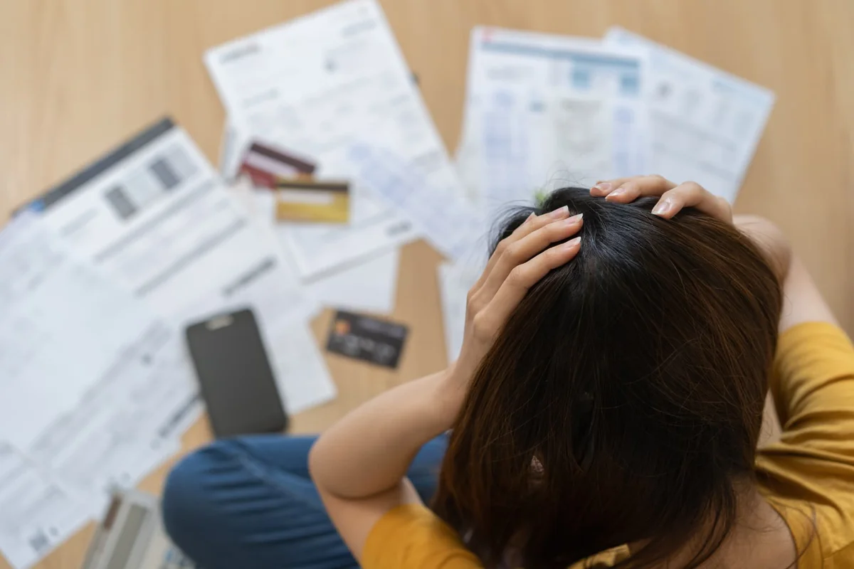 Stressed homeowner reviewing PG&E utility bills and credit cards on the floor