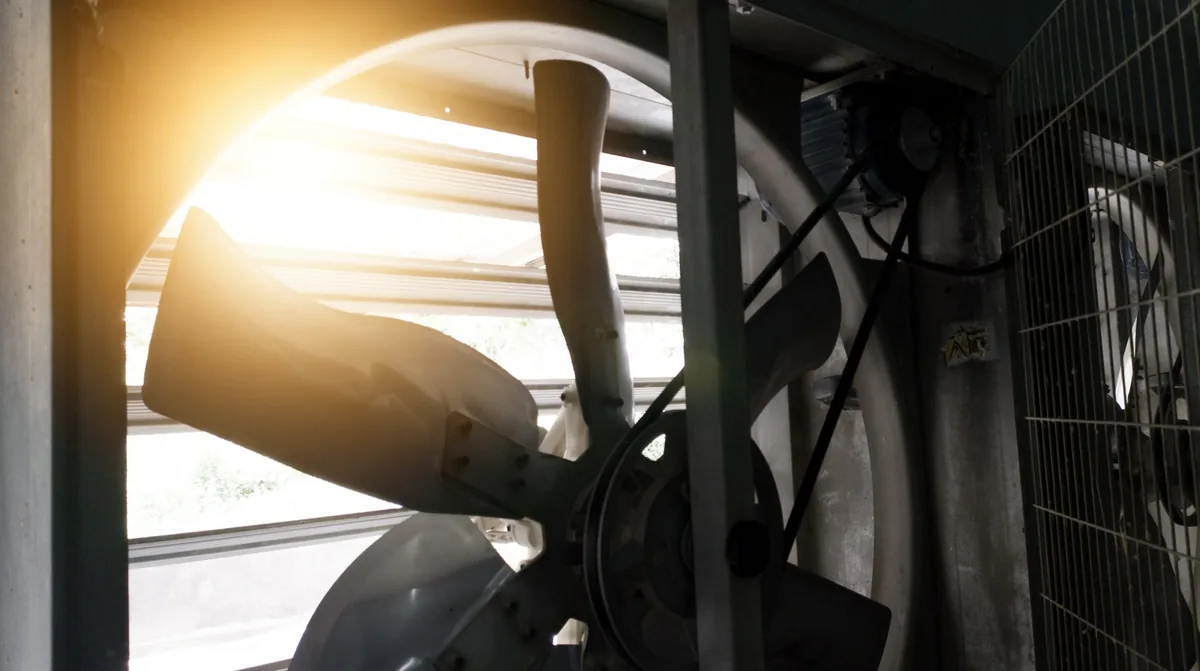 Large attic ventilation fan exhausting hot air with sunlight streaming through, Central Valley home