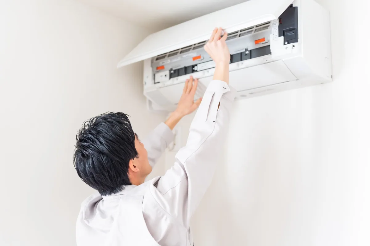 HVAC technician servicing a wall-mounted air conditioner, compared with whole house fan cooling